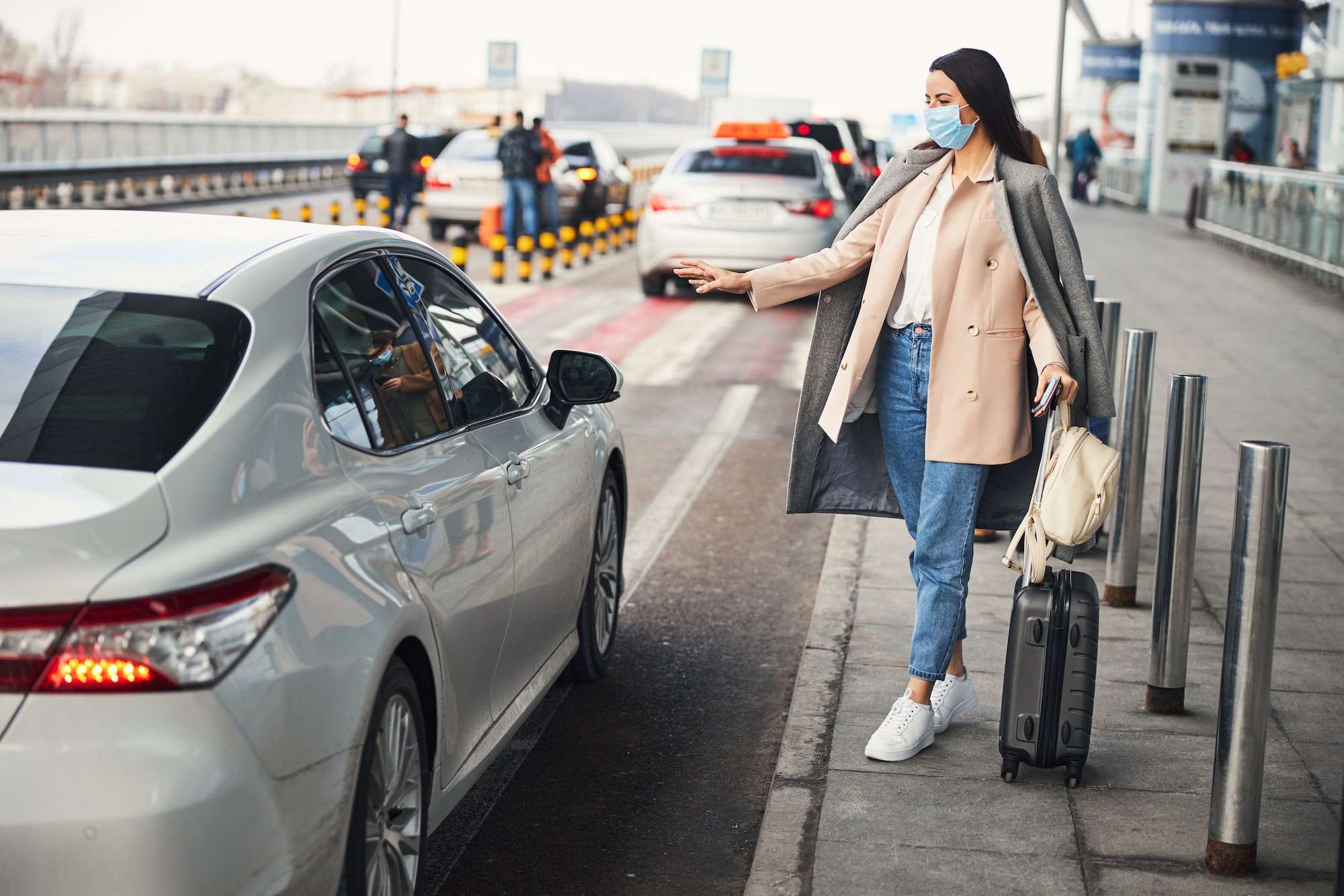 Stylish woman in medical mask taking cab at airport